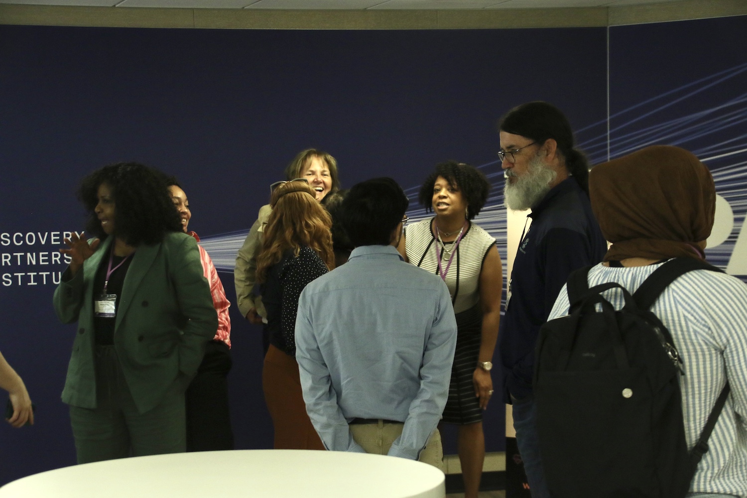 Symposium attendees mingling and discussing with each other against a wall with "Discover Partners Institute" signage.